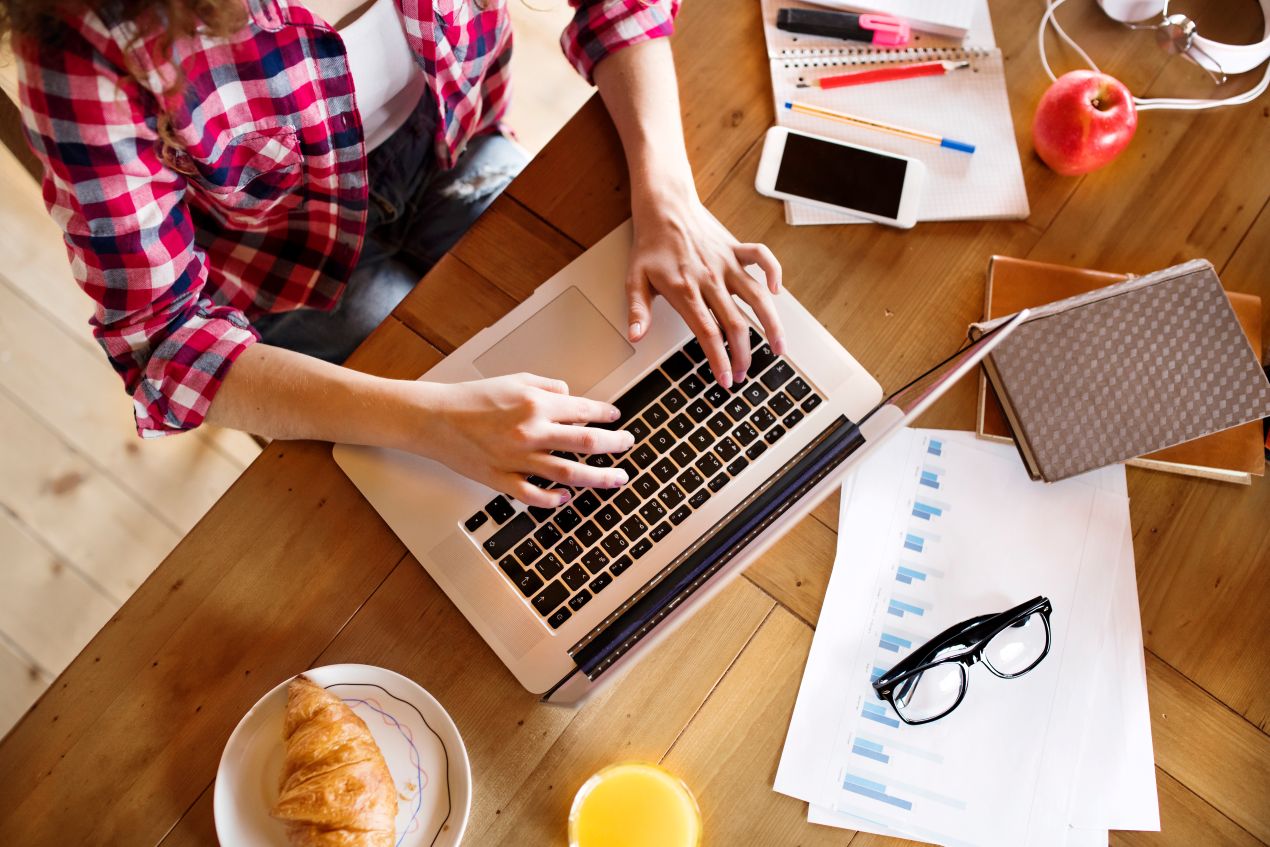 Eine Person arbeitet konzentriert am Laptop mit Notizbüchern, Diagrammen und Frühstück – effektives Zeitmanagement für Promovierende, die ihre Doktorarbeit schreiben lassen möchten.